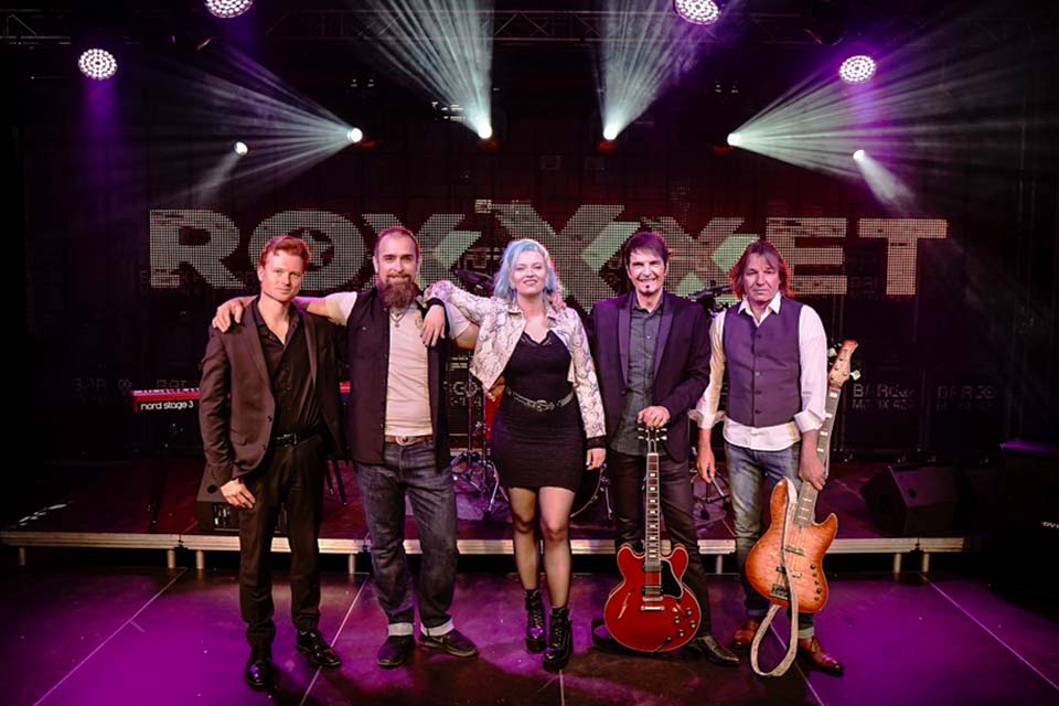 Das Bild zeigt fünf Musiker und eine Sängerin auf einer Konzertbühne.